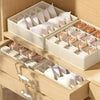 A set of white fabric organizers and folds displayed in a wooden drawer organizer.