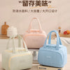A light pink and blue insulated quilted lunch bag is displayed next to a sliced fruit container.