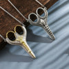 A pair of vintage stainless steel sewing scissors with gold accents hanging from a silver chain.