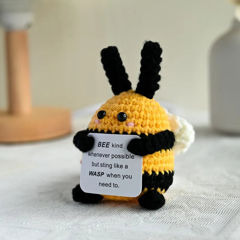 Handmade crochet bee kind doll with black and yellow yarn, featuring a sign that says bee kind whenever possible but sting li