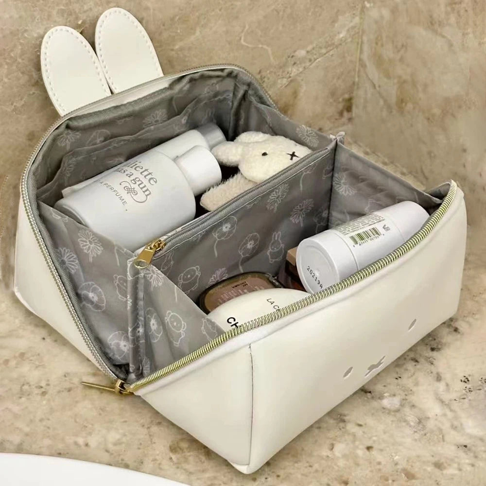 A beige cosmetic storage bag with a zipper and two white faux leather covers is shown on a marble surface.