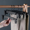 A hand is hanging space-saving adjustable clip hangers on a wooden rod, with a pair of light-colored pants visible.