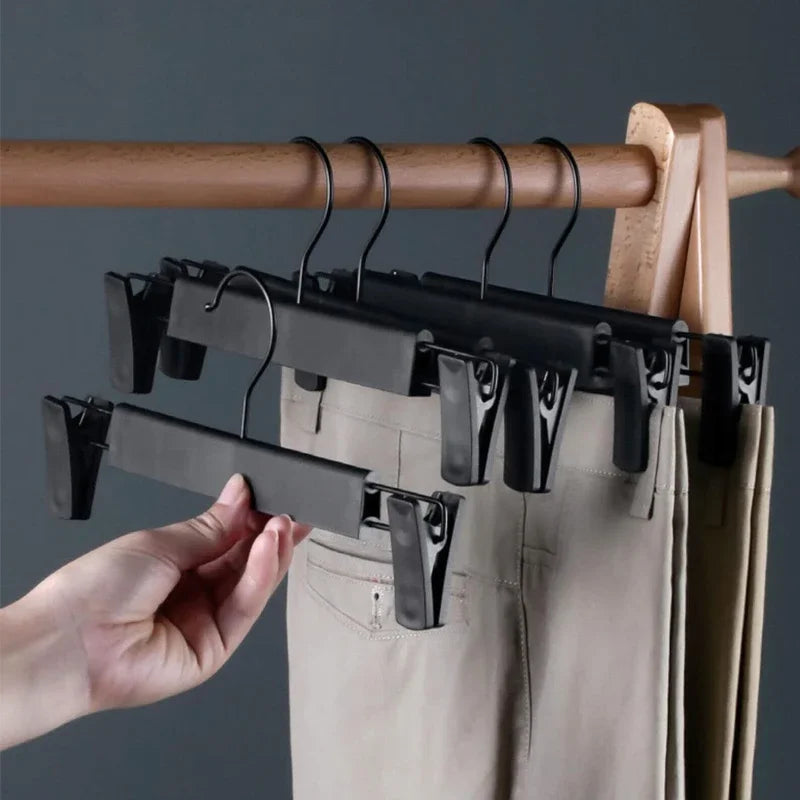 A hand is hanging space-saving adjustable clip hangers on a wooden rod, with a pair of light-colored pants visible.