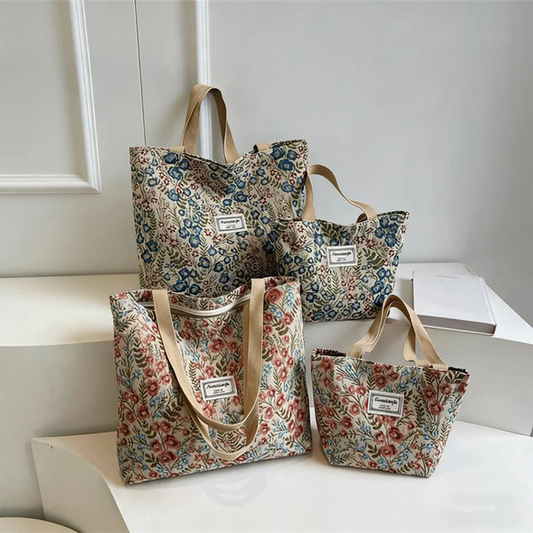 Tres bolsas tote de lona con bordado floral en varios tonos de verde y azul sobre una superficie blanca.