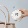 A hand holds a white portable denture case with a cleaning brush storage feature, next to a light pink handbag.