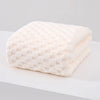 A white, textured plush bath towel is shown lying on a white surface.