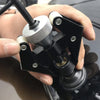 A hand holds a black two-arm puller tool with a silver threaded end, used for alternator and bearing removal.