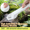 A hand holds a white handheld insect catcher with a transparent viewing window, positioned among green moss and foliage.