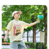 A child is playing with a yellow t-shirt featuring a cat design while holding a green flying saucer toy.