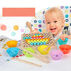 A baby is interacting with a wooden bead maze puzzle and various wooden utensils for toddlers.