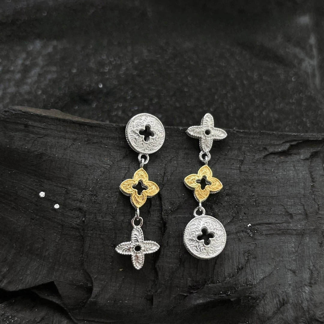 A pair of silver and gold two-tone clover stud earrings resting on a dark, textured surface.