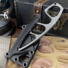 A compact stainless steel neck knife is shown resting on a tan fabric with various leather-like shapes.