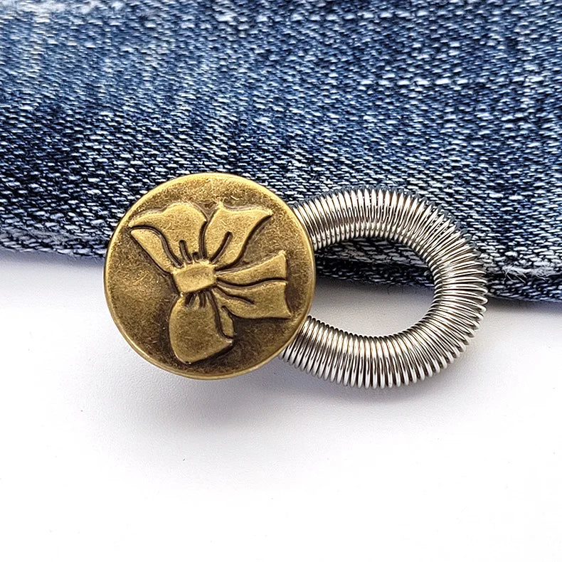 A round brass button with a floral design and silver wire attached, resting on a denim fabric.