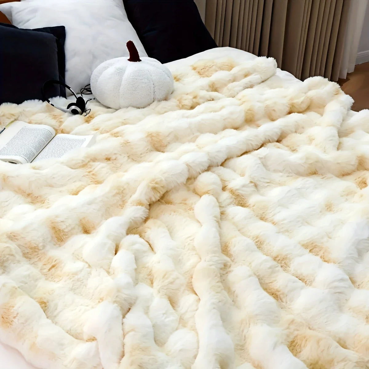 Flauschiger cremefarbener Kunstkaninchen-Fleece-Decke über einem dunklen Sofa mit einer weißen Kürbis und einem Buch.