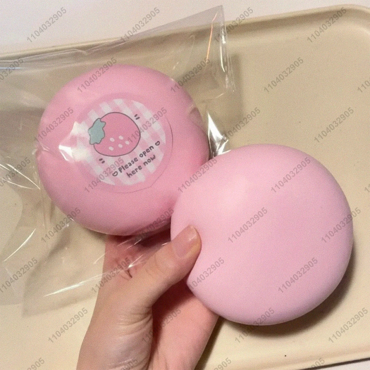 A pink extra-large slow-rising milk bread squishy is held in a clear plastic bag on a light surface.