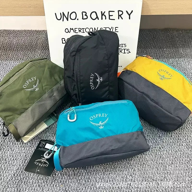 Collection de sacs de toilette pliables et imperméables Osprey noirs, vert olive, jaune et bleu sur une surface grise.