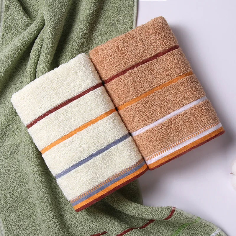 A set of three bath towels in shades of beige, orange, and green are displayed on a light surface.