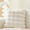 A fluffy white faux fur decorative pillow resting on a light-colored surface.