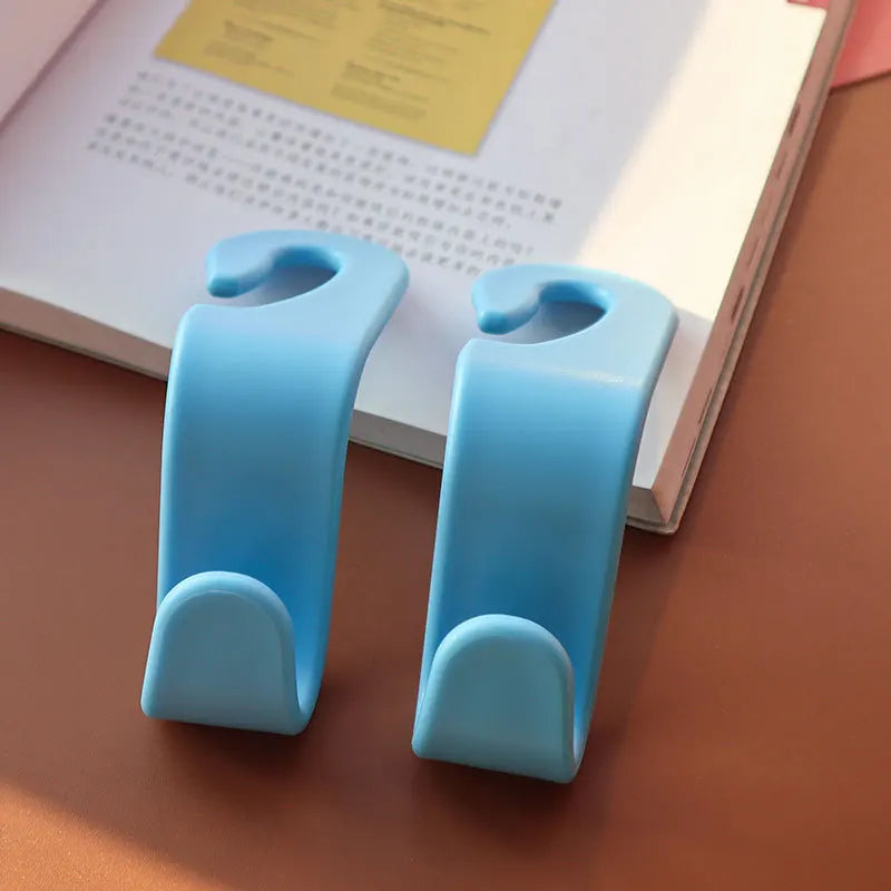 A pair of light blue universal car seat headrest hooks resting on a white book.