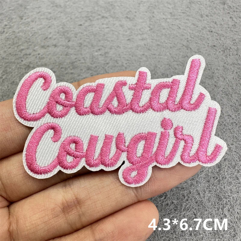 Pink embroidered patch with the text Coastal Cowgirl on a hand