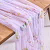 Light purple tulle table runner featuring delicate floral embroidery on a wooden table.