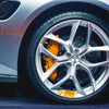 Close-up of a silver car wheel with an orange brake caliper and reflective safety stickers visible.