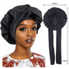 A black silky satin sleep cap with a wide band shown on a model's head and next to its hanging form.