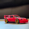 A red 1:64 scale alloy car wheel and tire set with yellow rims resting on a light surface.