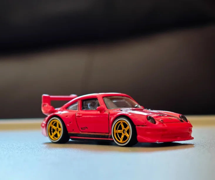 A red 1:64 scale alloy car wheel and tire set with yellow rims resting on a light surface.