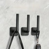 Three black no-punch adhesive hooks with leather cord attachments mounted on a white wall.