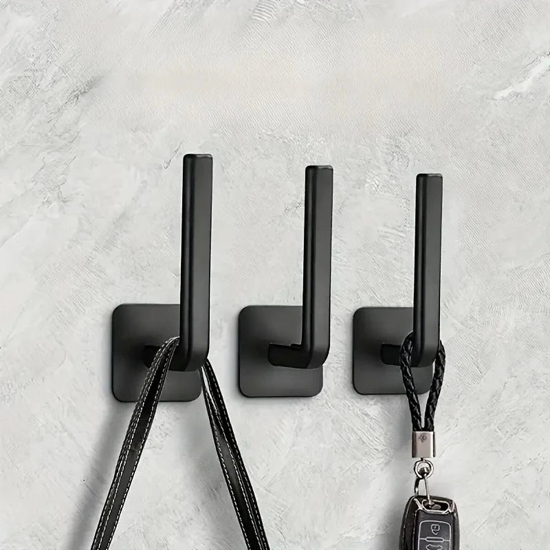 Three black no-punch adhesive hooks with leather cord attachments mounted on a white wall.