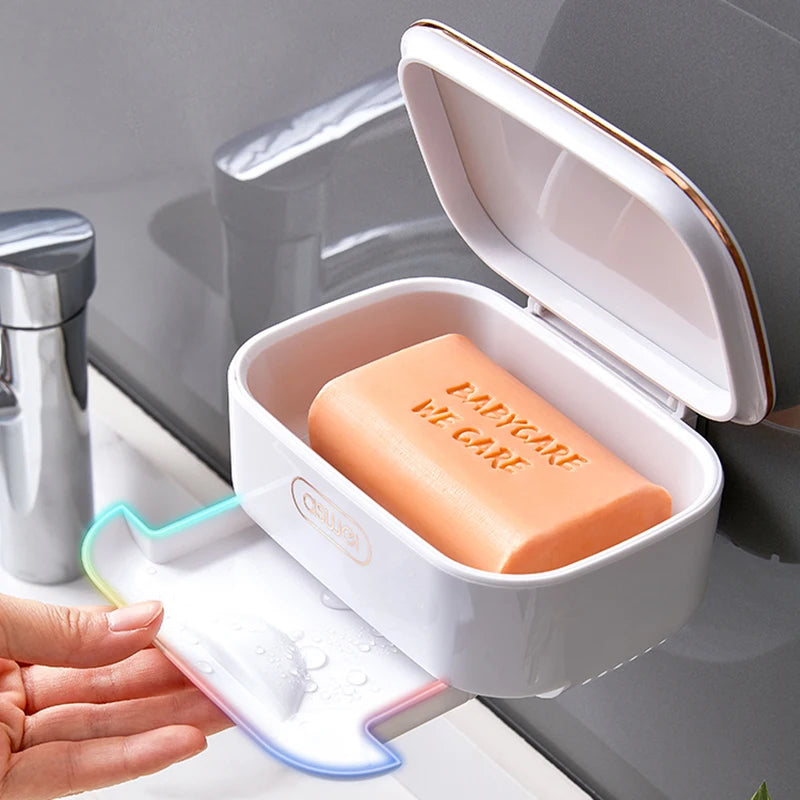 A hand holds a white two-tier draining soap holder with an orange bar of baby care soap inside.