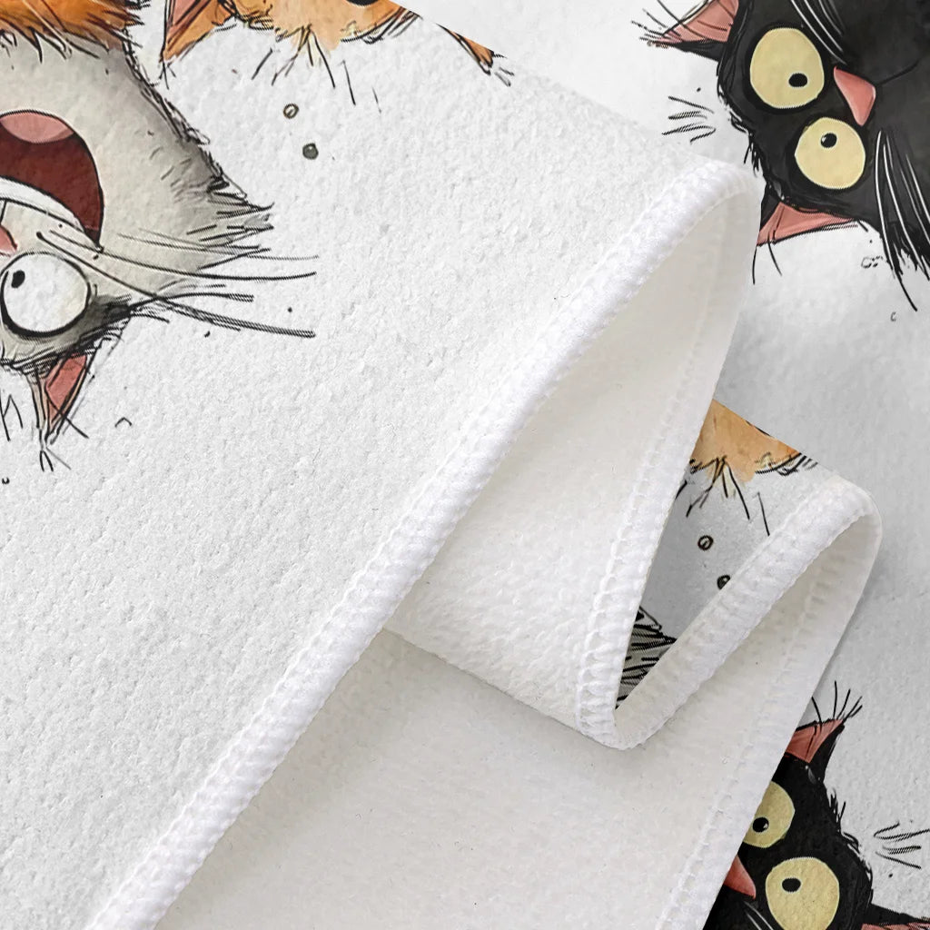 A close-up of a white kitchen towel featuring a cartoon cat design with large eyes and whiskers.