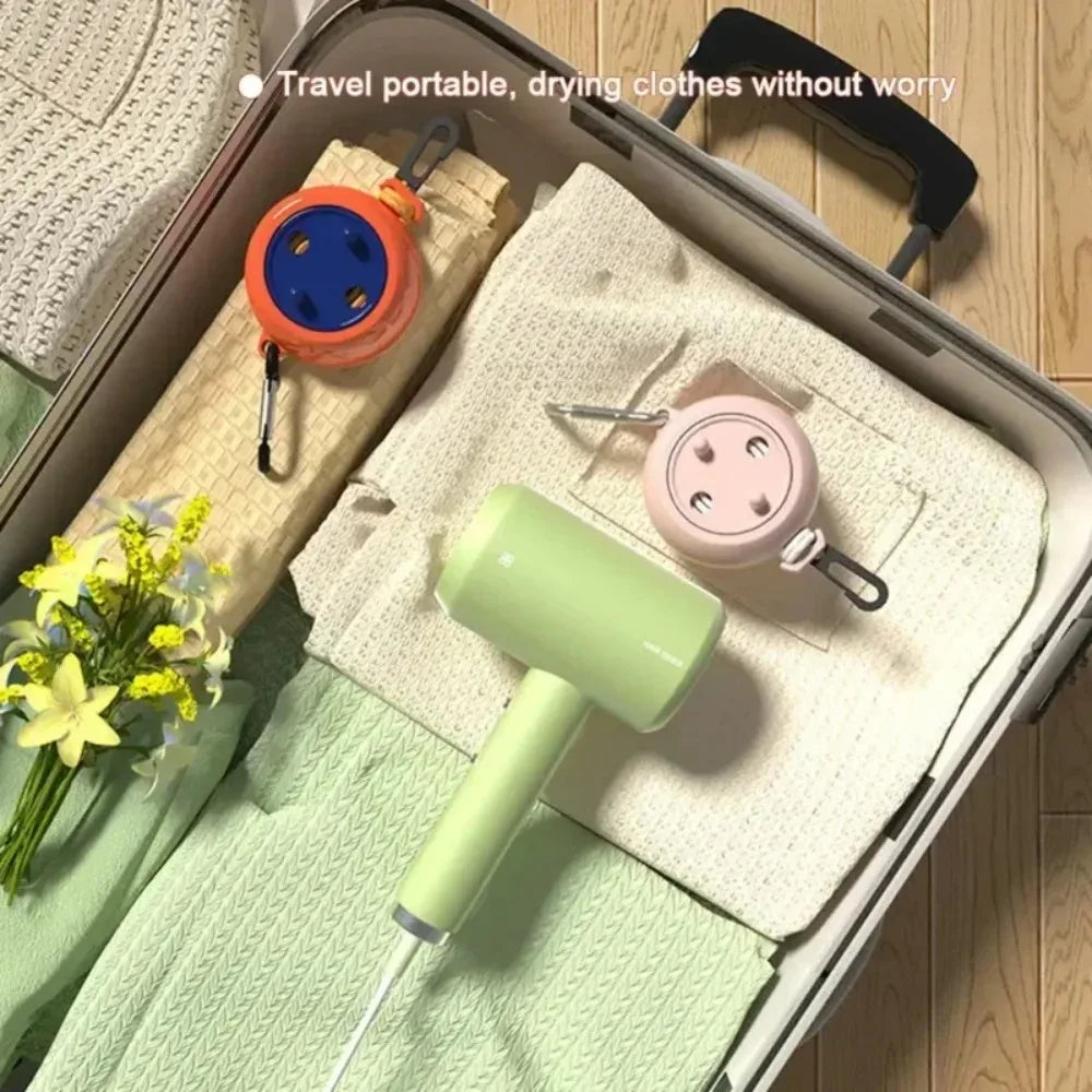A portable retractable drying clothesline with a green handle and pink clothespins is shown inside a suitcase.