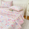 Pink and white floral quilted bedspread with pink pillows on a white bed.