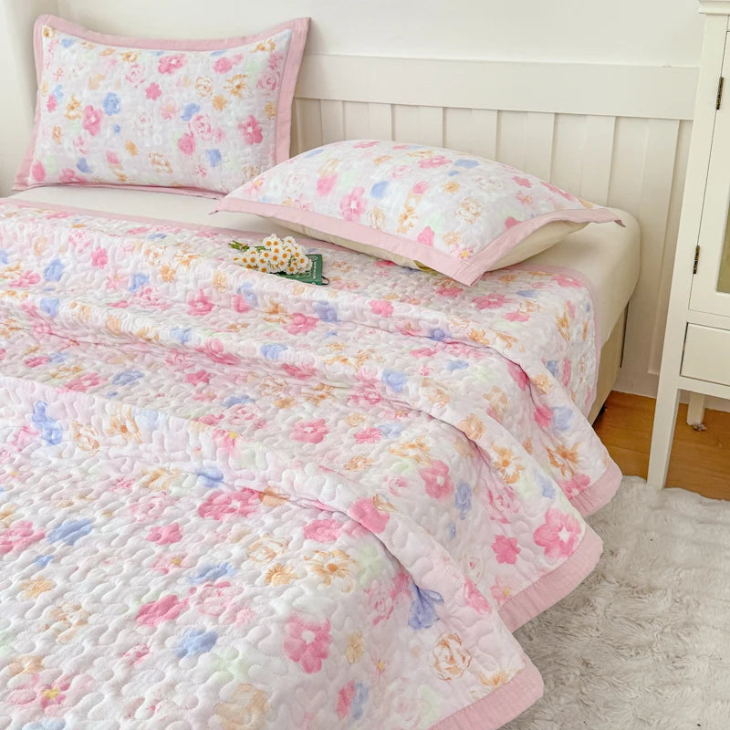 Pink and white floral quilted bedspread with pink pillows on a white bed.
