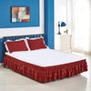 A white bed with a deep red ruffled skirt on the bed and blue accent walls.