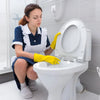 A woman wearing yellow gloves is cleaning a white toilet bowl with a pumice stone block.