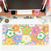 A colorful floral mouse pad featuring pink, yellow, and green flowers placed on a wooden desk with a computer setup.