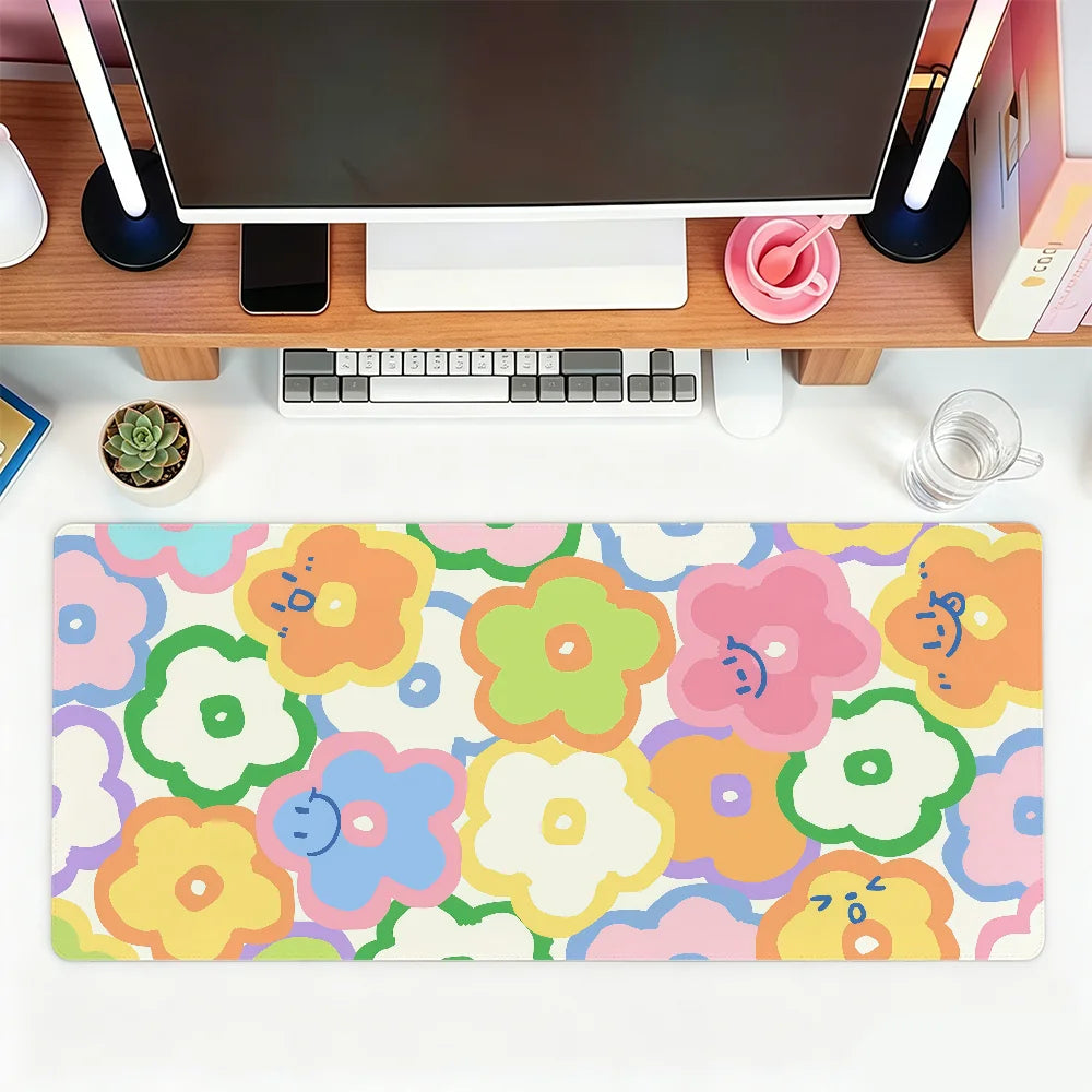 A colorful floral mouse pad featuring pink, yellow, and green flowers placed on a wooden desk with a computer setup.