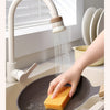 A hand is using a kitchen faucet sprayer to rinse food in a frying pan.