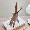 A beige resin hand planter and pen holder with wooden sticks resting on a white book.