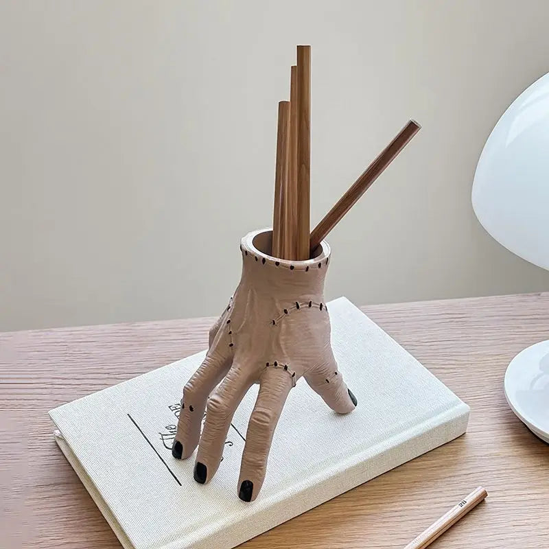 A beige resin hand planter and pen holder with wooden sticks resting on a white book.