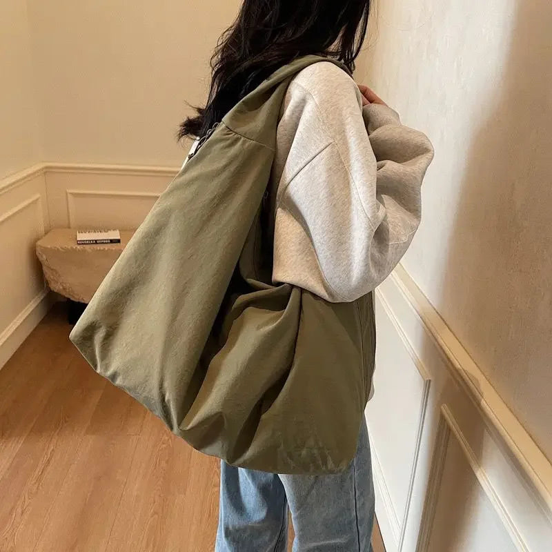 A person is holding a large olive green lightweight nylon tote bag with a secure zipper closure.