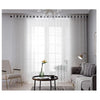 White embroidered sheer voile curtain panels hanging over a window in a modern living room.