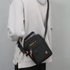 A black crossbody bag with an adjustable strap is shown hanging from a light gray hoodie.