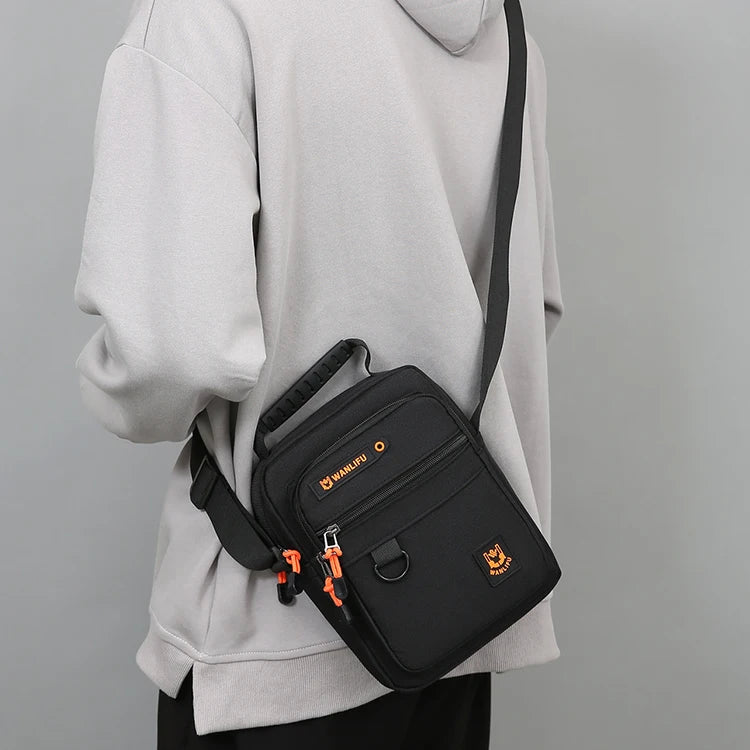 A black crossbody bag with an adjustable strap is shown hanging from a light gray hoodie.