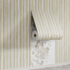 Roll of striped wallpaper featuring vertical light gray and gold stripes mounted on a white wall.