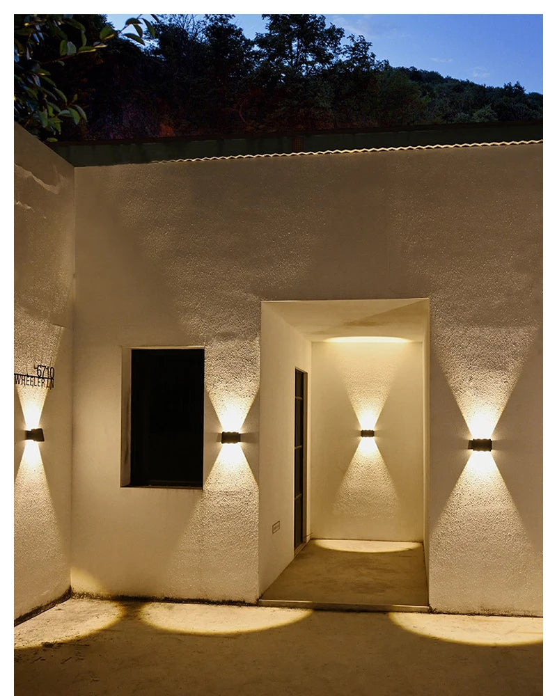 A white stucco wall features several upward-pointing LED lights illuminating an entryway.