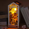 A miniature DIY book nook kit featuring a detailed bookshelf room scene with lighting and decorative elements.